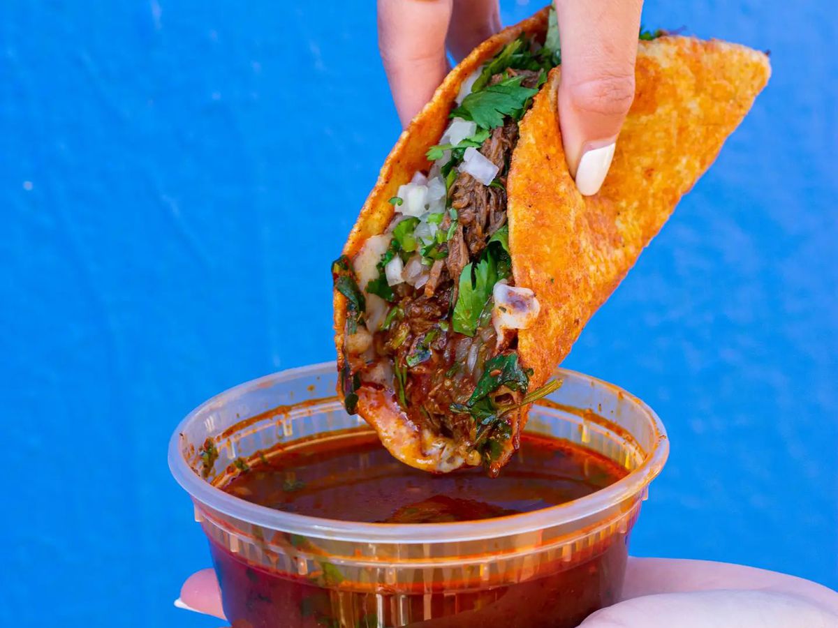 A person dipping a taco into a short plastic container of broth. 