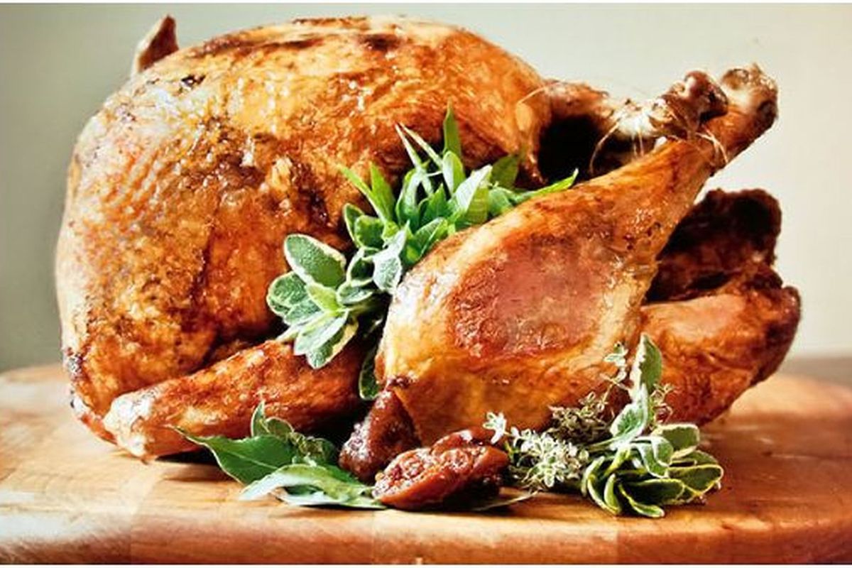 Deep-fried turkey decorated with sage on top of a wooden cutting board.