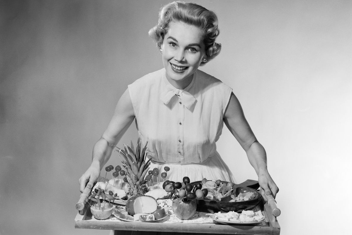 A black and white photo of a woman holding a tray of food
