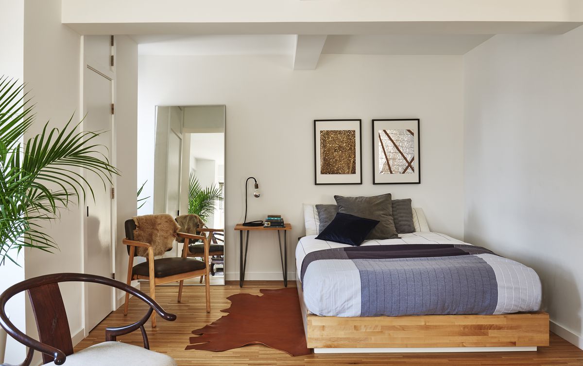 A bedroom has a platform bed with storage drawers underneath and a midcentury modern armchair.
