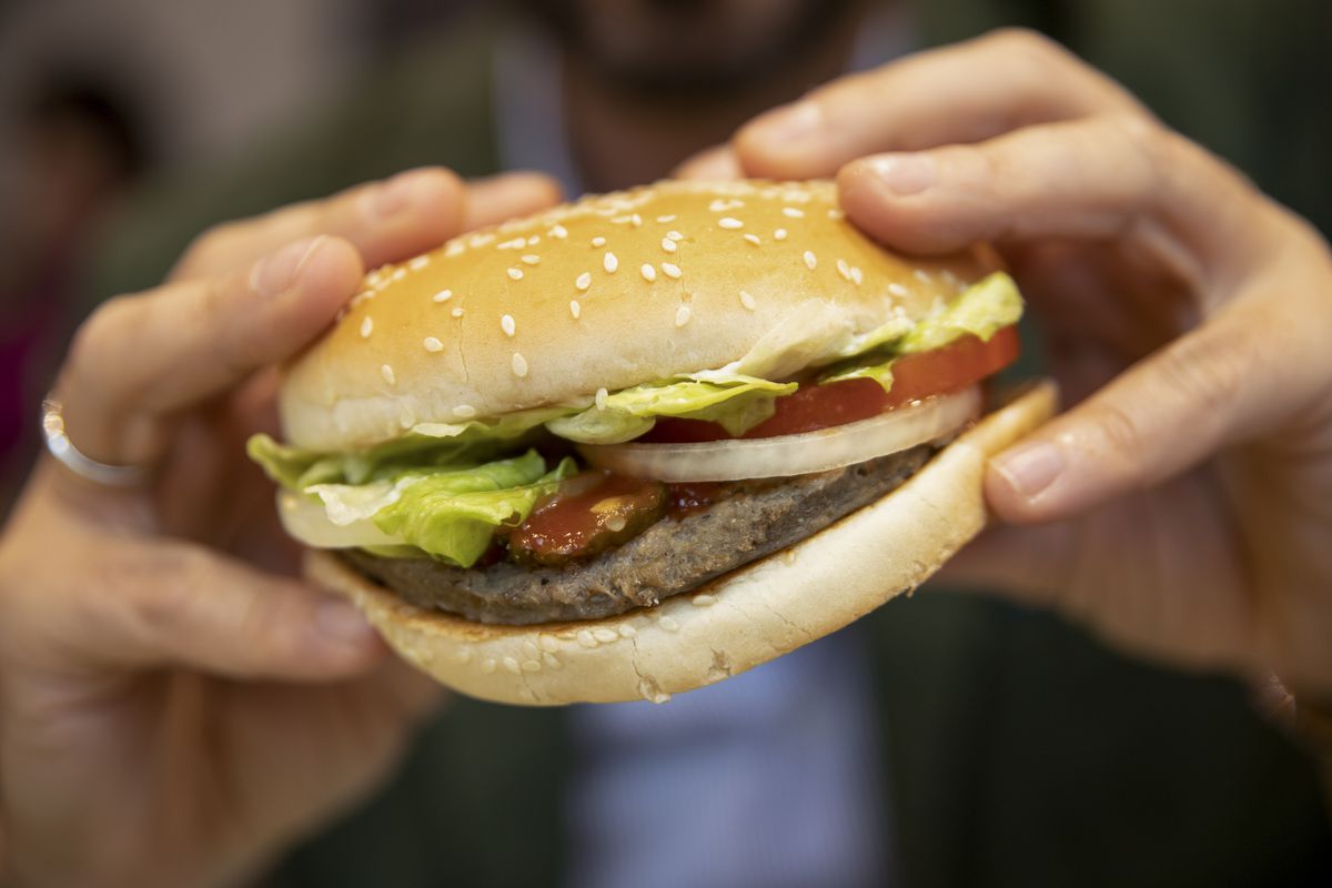 Hands holding a hamburger in a bun.