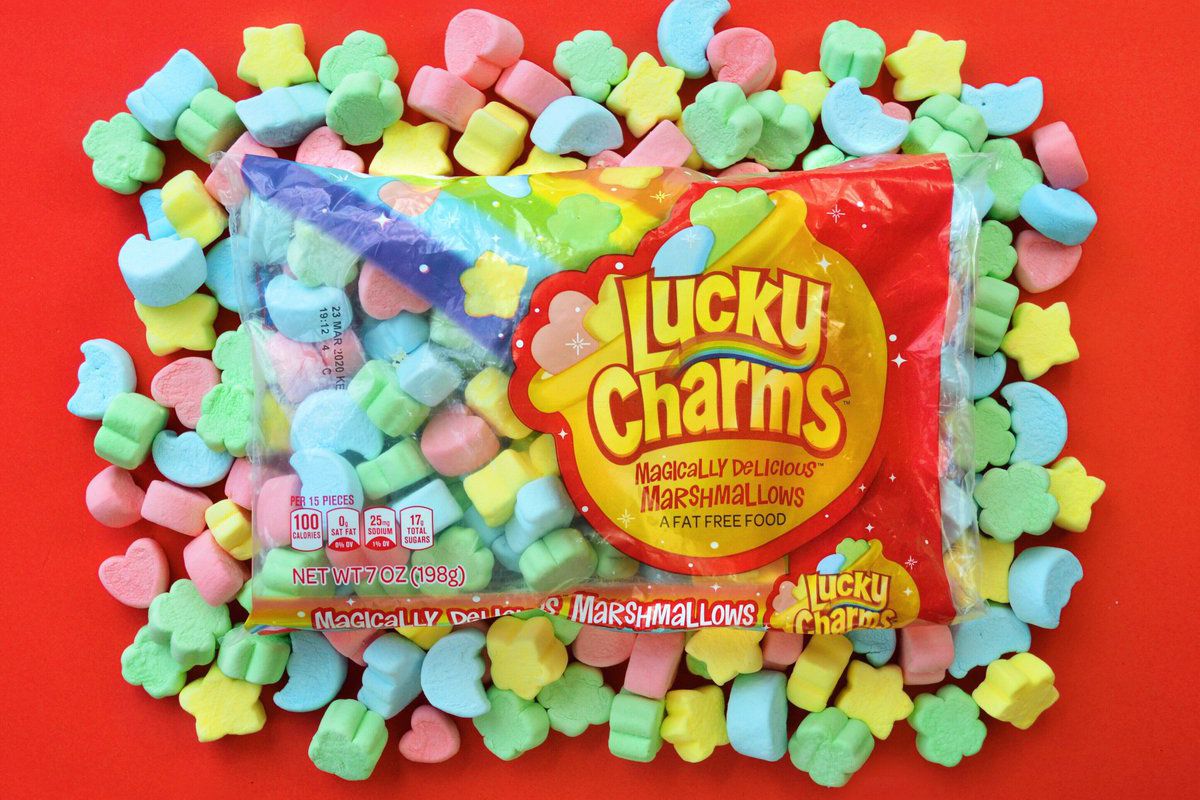 A package of Lucky Charms marshmallows on top of a bed of colorful Lucky Charms marshmallows, on a red background.