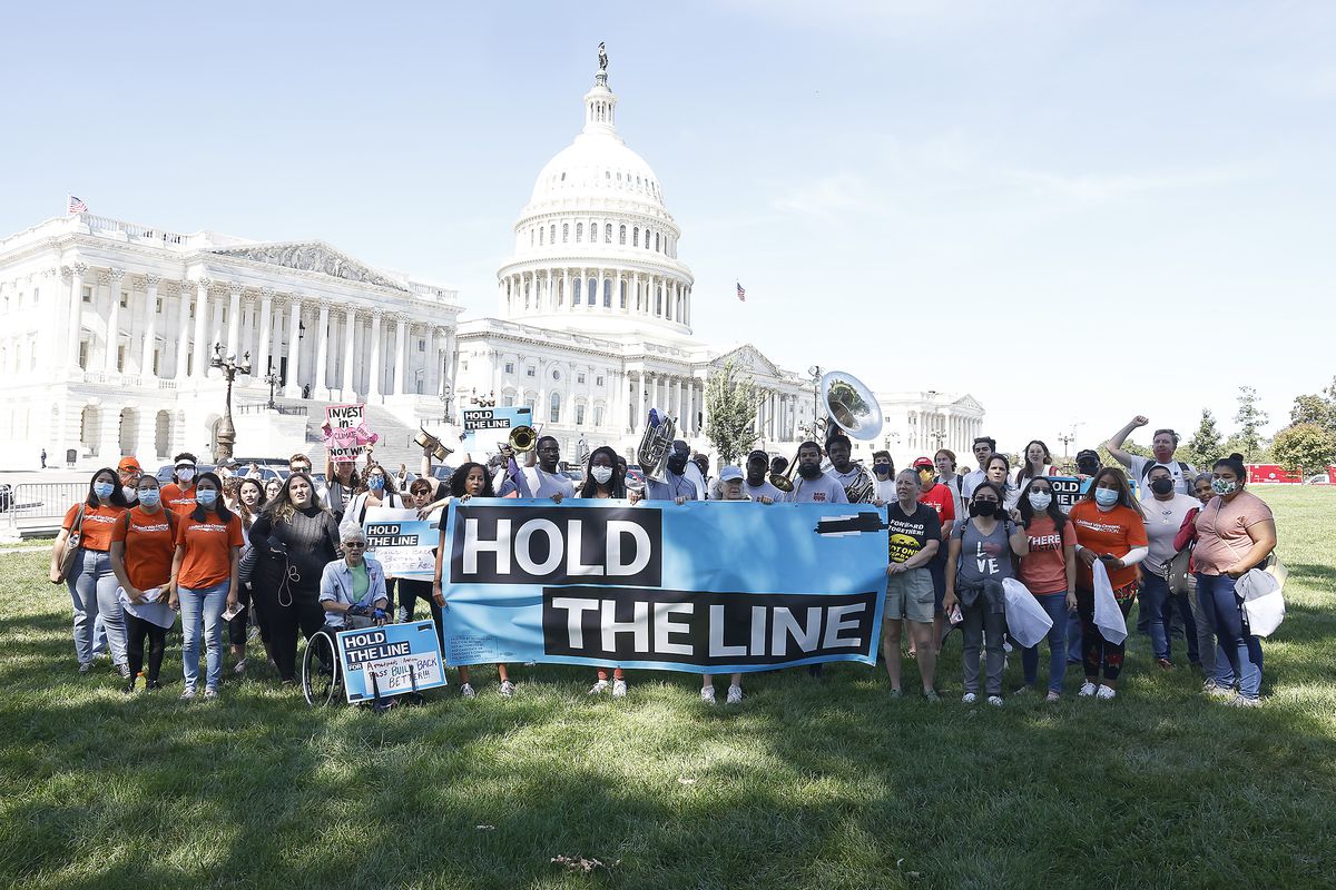 Demonstrators stand on the lawn in front of the US Capitol holding a banner that reads “hold the line.”