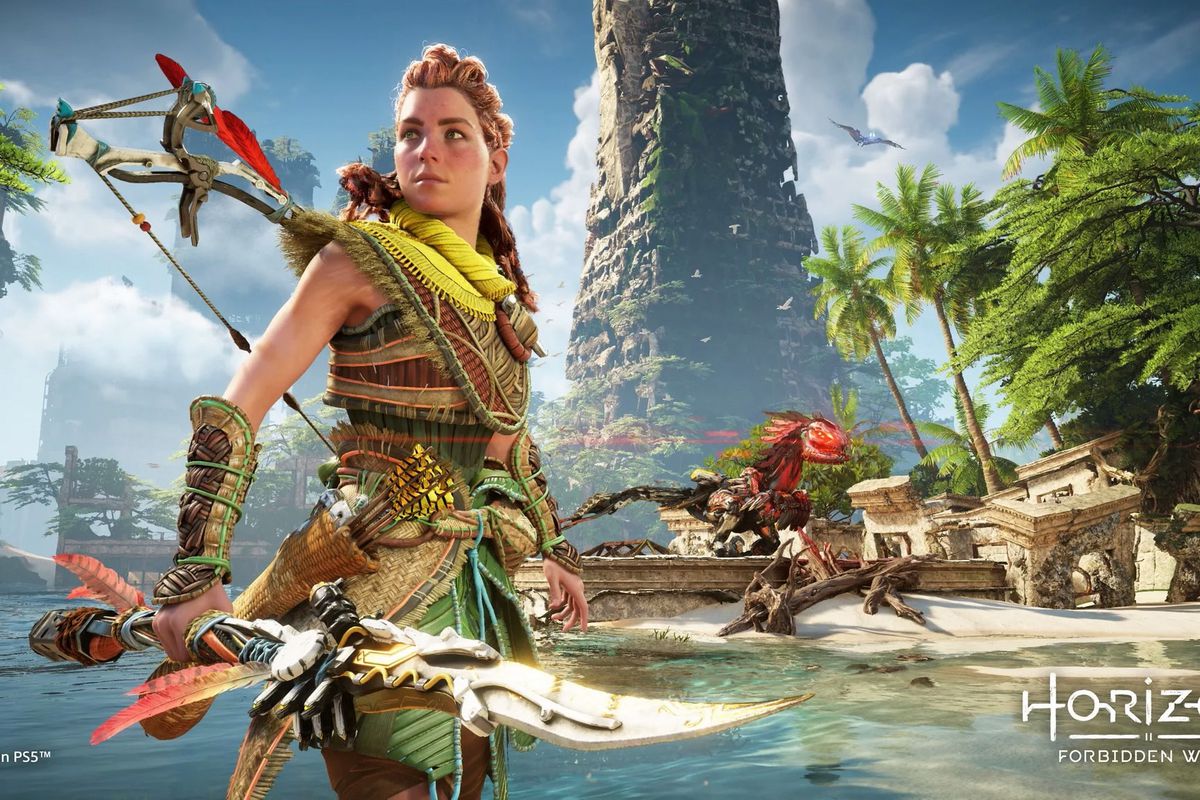 Aloy standing on a beach holding a spear looking into the distance while a Machine prowls in the background in Horizon Forbidden West