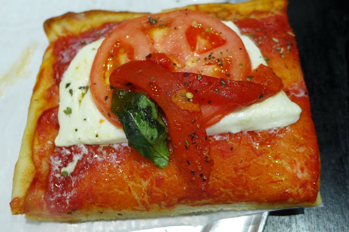 A square red slice with slab of white cheese and slice of fresh tomato on it.
