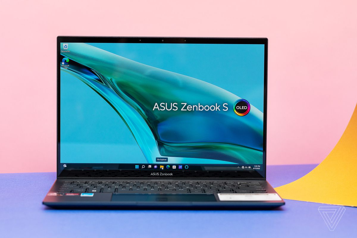 Asus Zenbook 13 S OLED atidaromas ant mėlynos ir rožinės spalvos paviršiaus.  Ekrane rodomas Asus Zenbook S OLED logotipas virš vandens srovės mėlyname fone.
