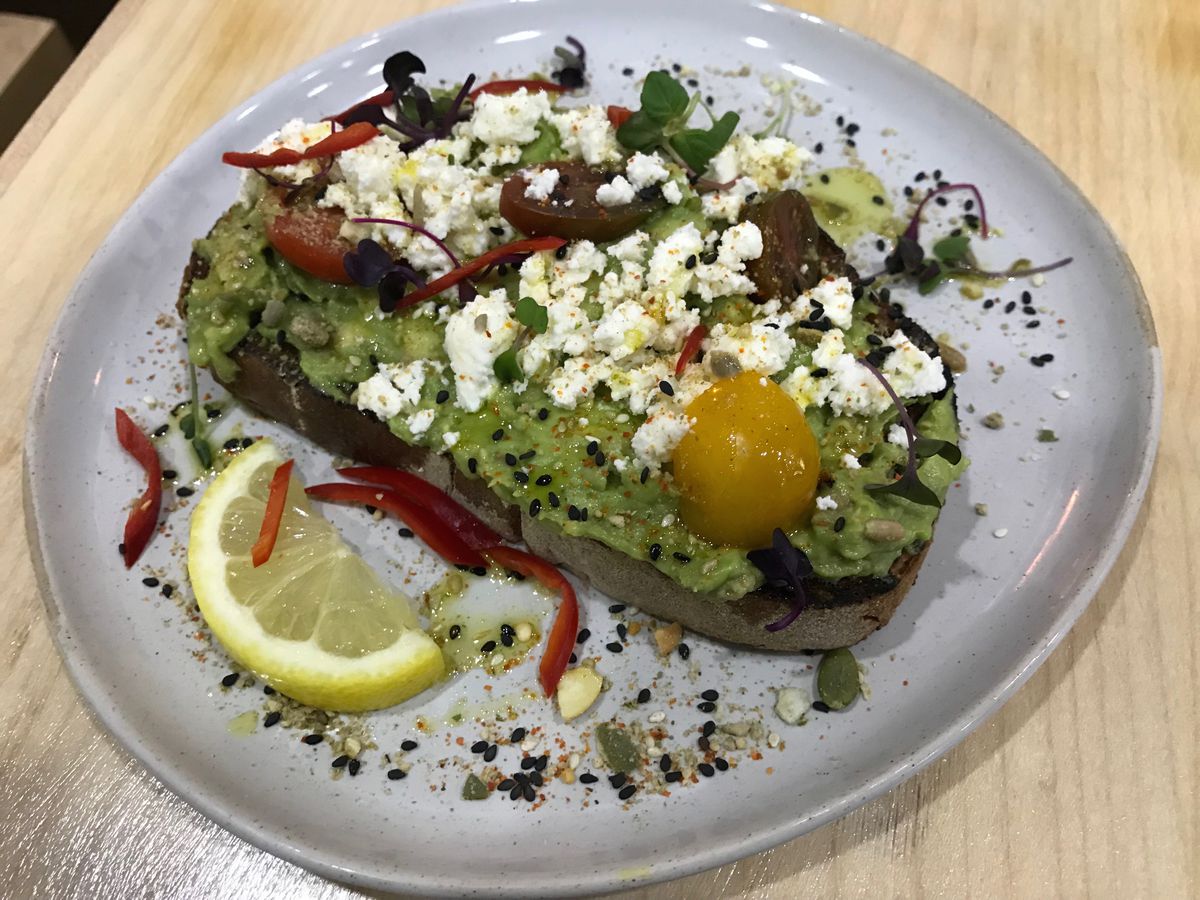 Avocado toast is topped with lemon, cheese, tomato, egg, and black sesame seeds