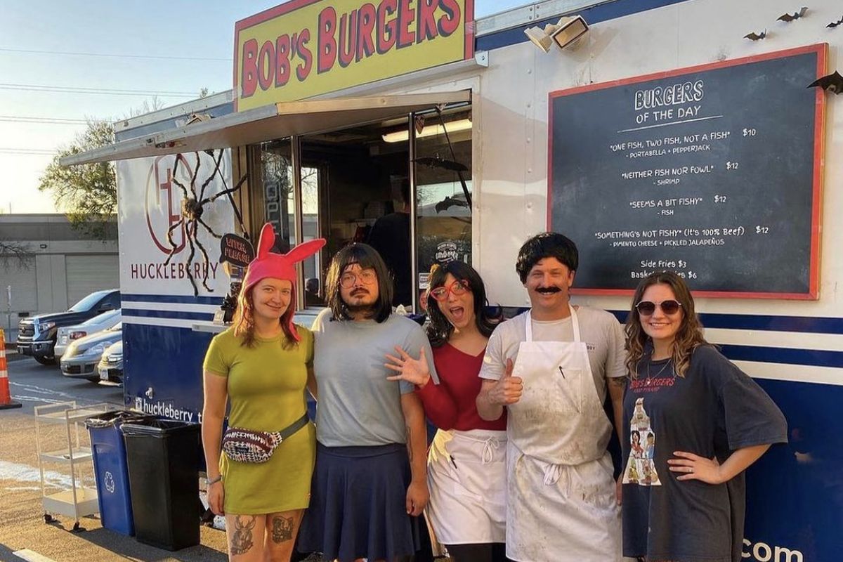 A food truck with a sign that reads “Bob’s Burgers” and people standing in front of it in costumes.