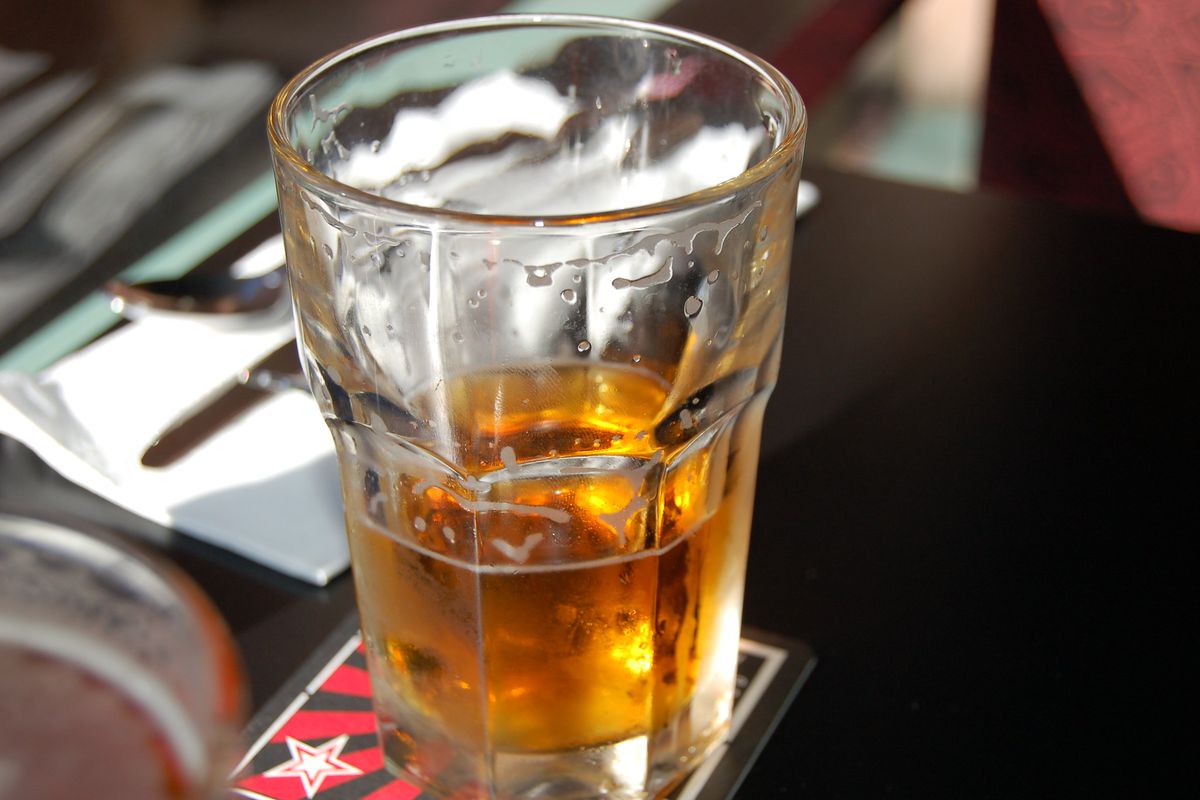 A half-drank beer sits on a dark bar.