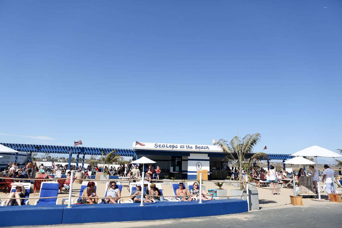 A daytime beach restaurant with loungers, blue walls, umbrellas, and lots of sky.