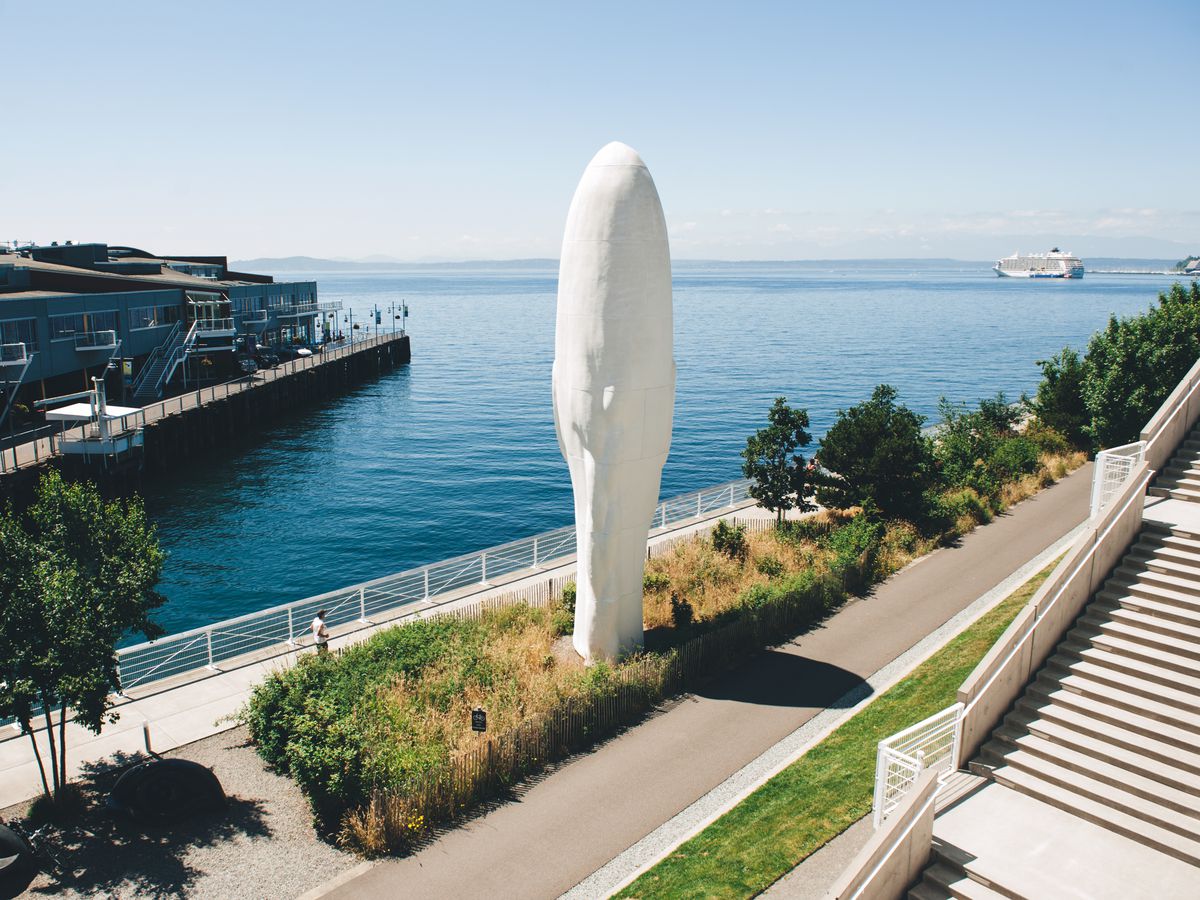 A sculpture of a narrow head on a waterfront boardwalk. Stairs lead up to the right.