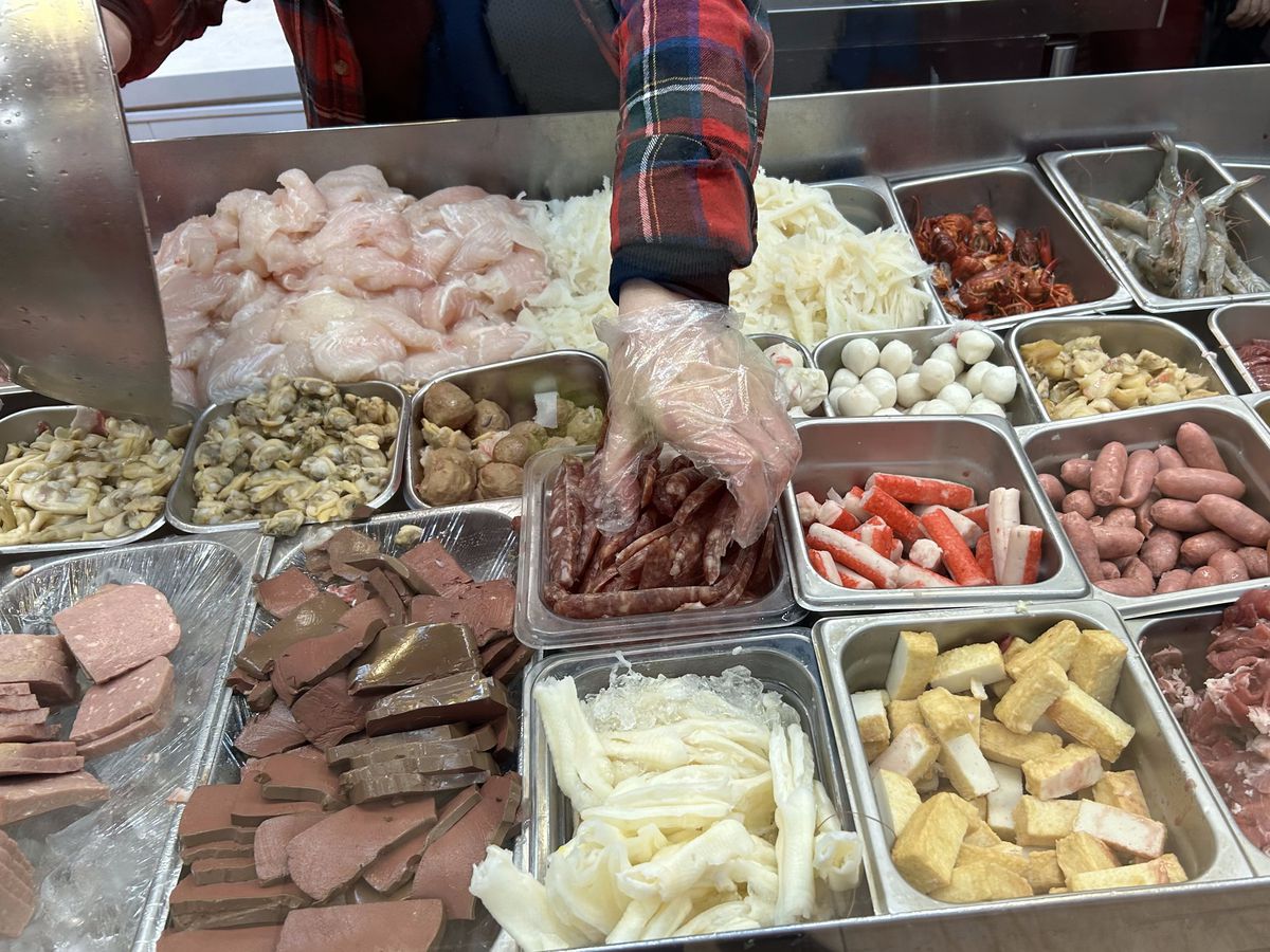 A gloved hand grabs at Chinese sausage, rolled meat, and hot dogs.