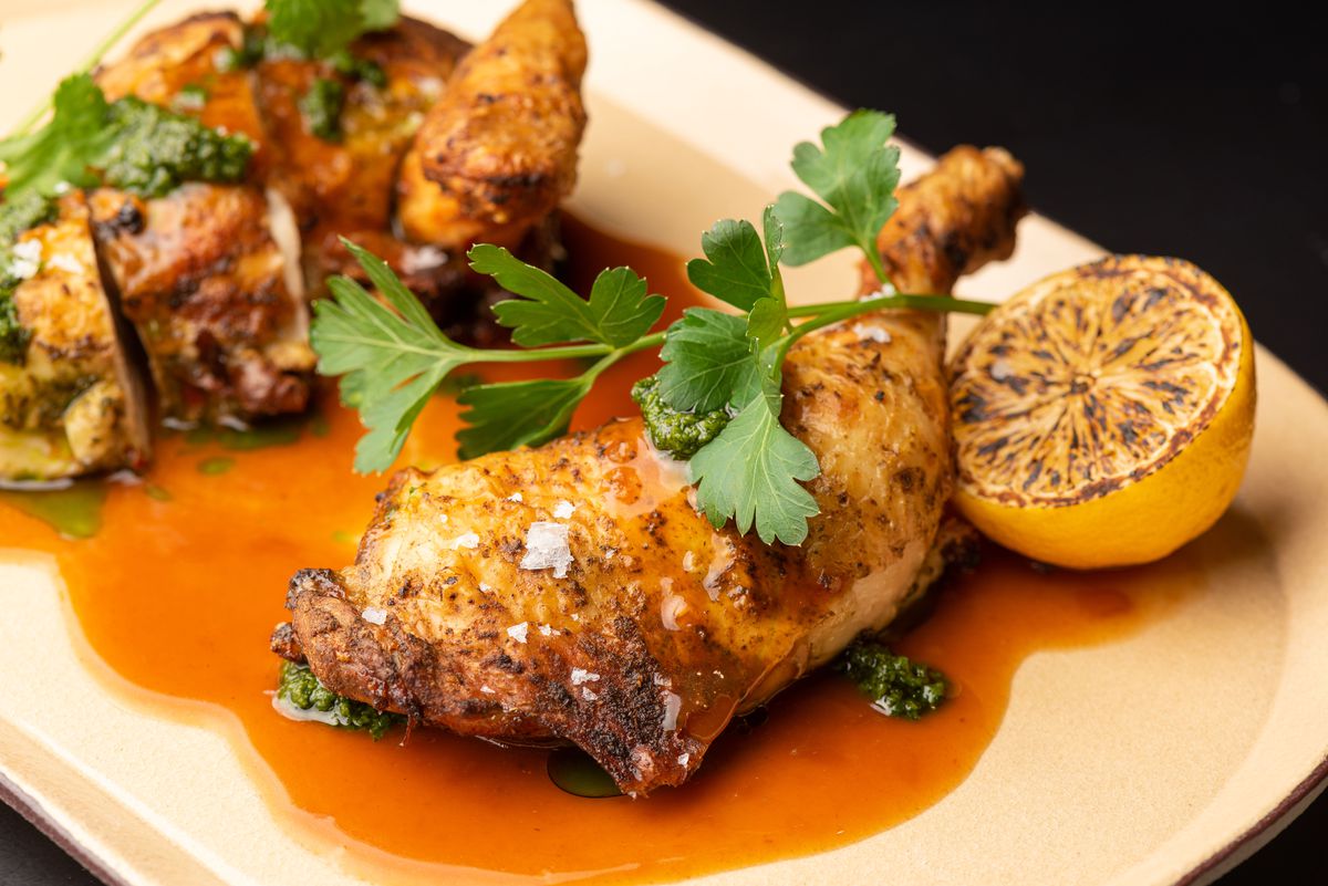 A leg of roasted chicken in a golden jus on a plate.