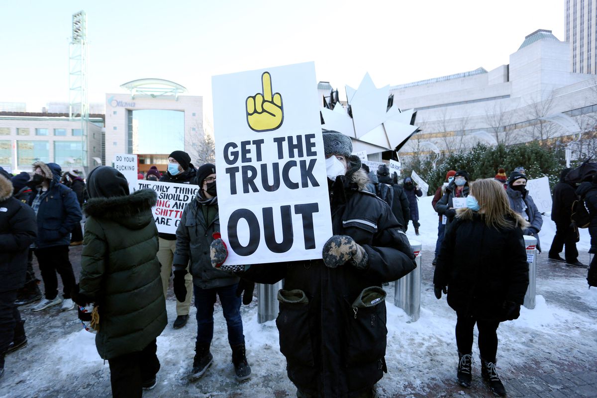 A protester holds a sign with a raised middle finger and the words “get the truck out.”