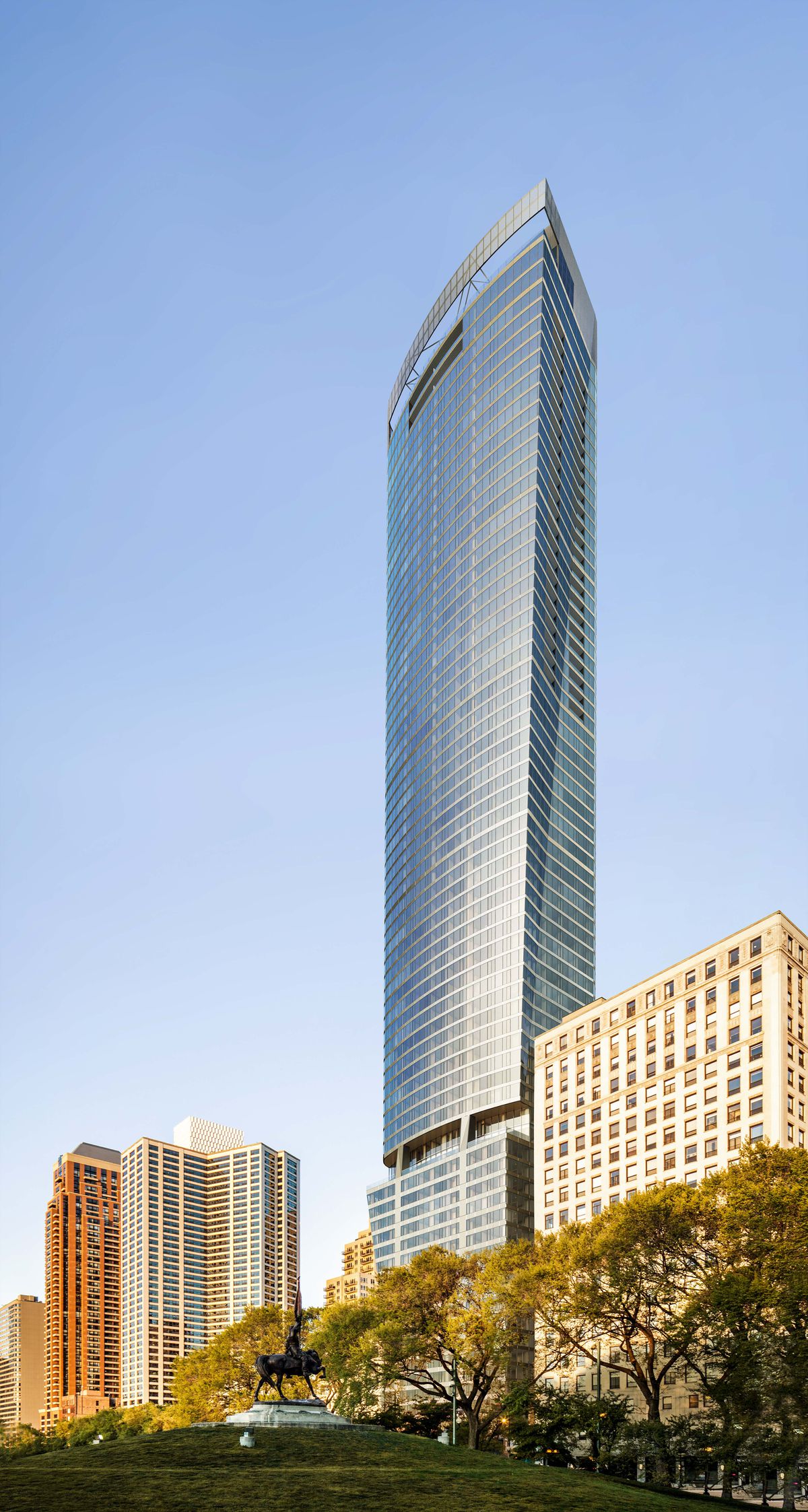 A ground-level rendering of a curving glass skyscraper viewed from a grassy green space. The tower is much taller than the buildings around it.