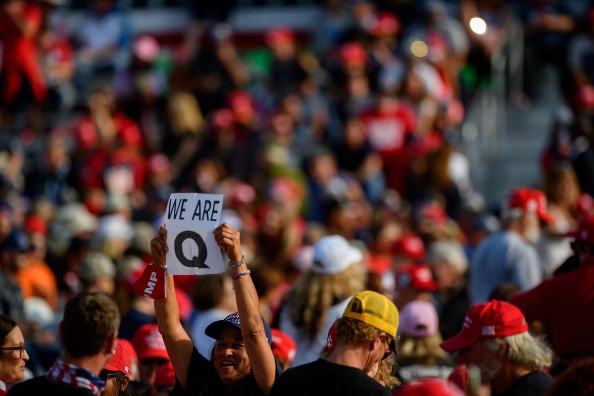 A person in a crowd holds up a sign that reads “We are Q.”