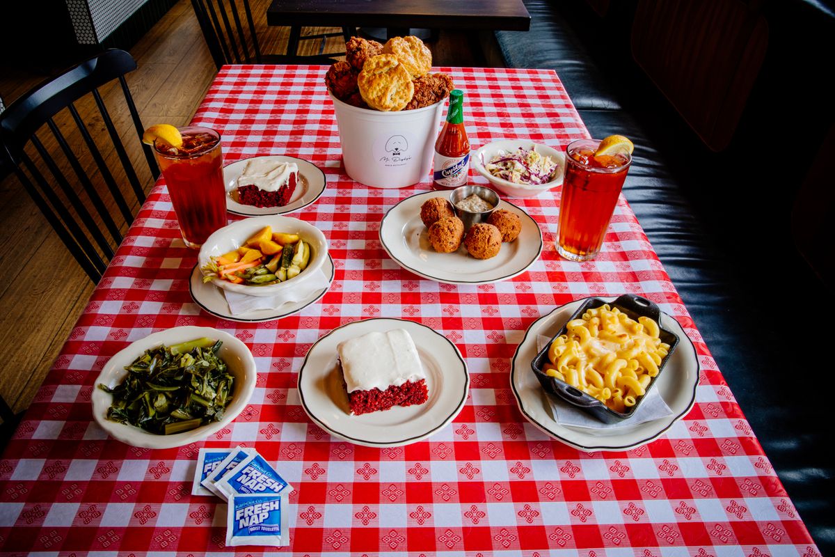 A gingham tablecloth covers a table filled with a spread of food, including fried chicken, mac and cheese, and red velvet cake, from Mr. Digby’s in San Francisco