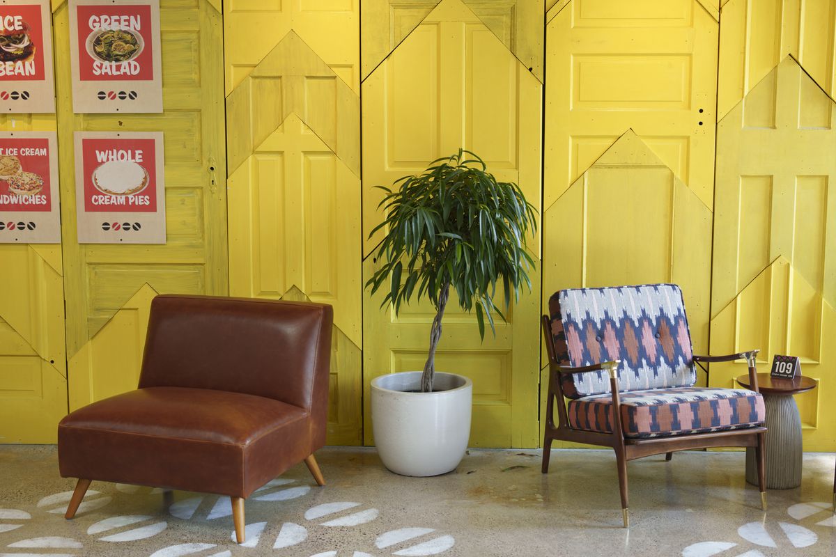 Two chairs and a potted plant in front of a bright yellow wall. 