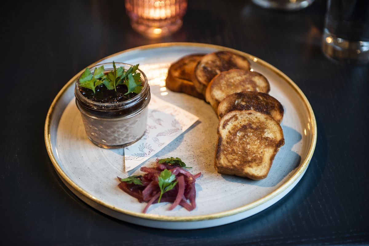 A round plate with slices of toasted milk bread, a glass jar of chicken liver mousse with cherry jam, pickled red onions.