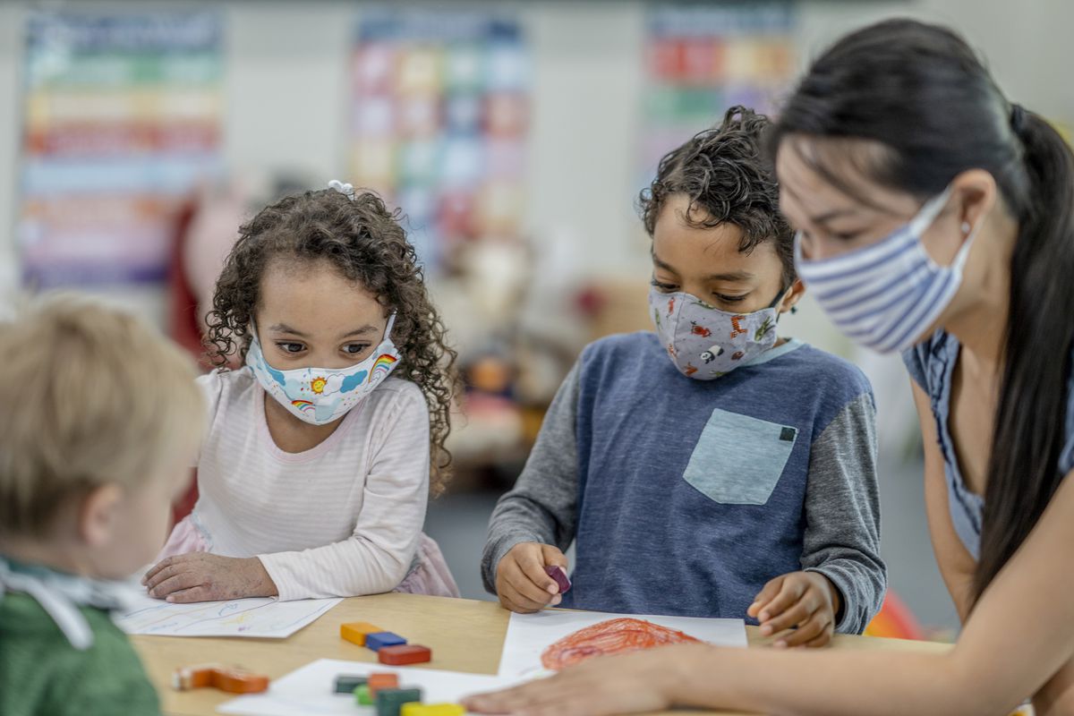 Children coloring at a table while wearing protective face masks.
