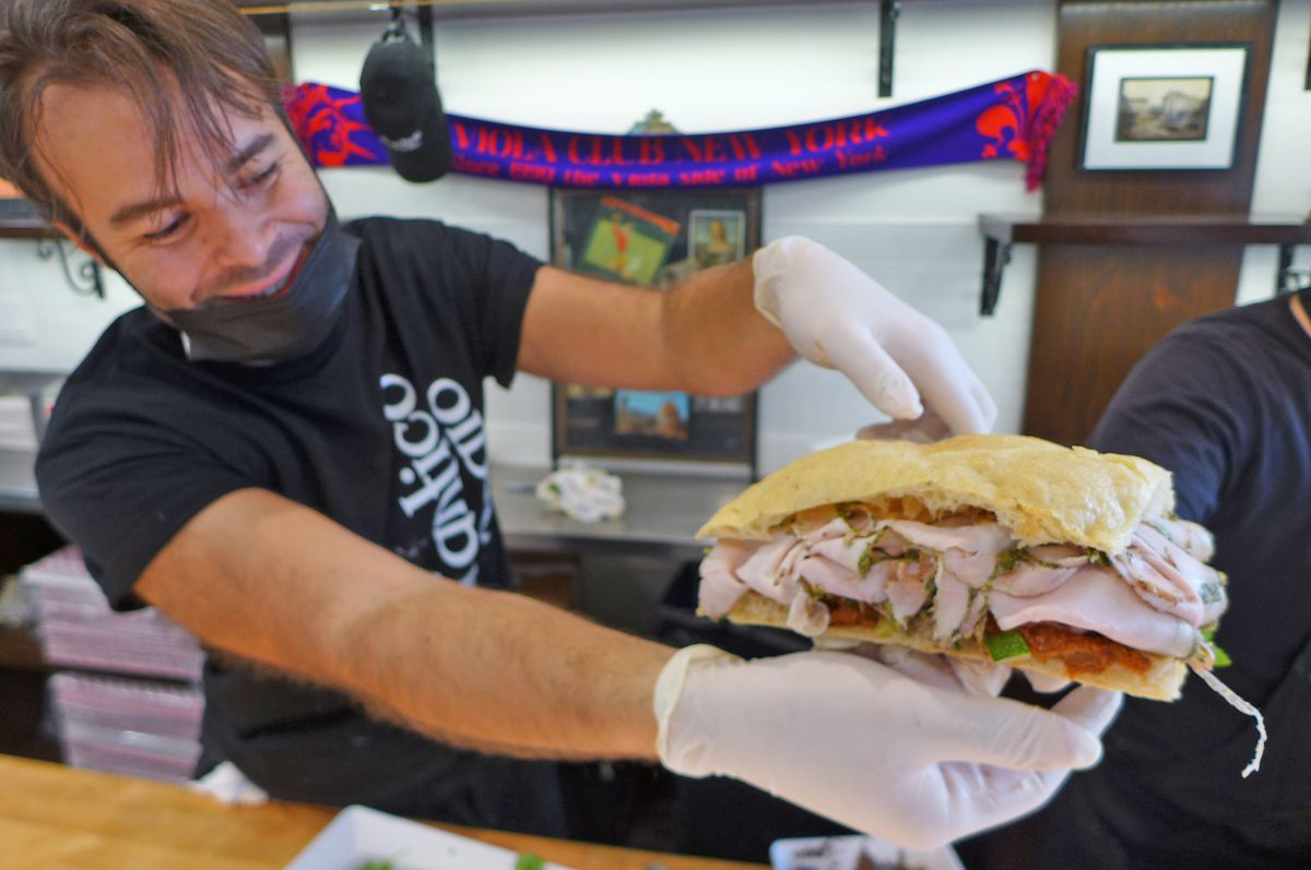 A man in a black t-shirt holds up an overstuffed sandwich on two flatbreads.