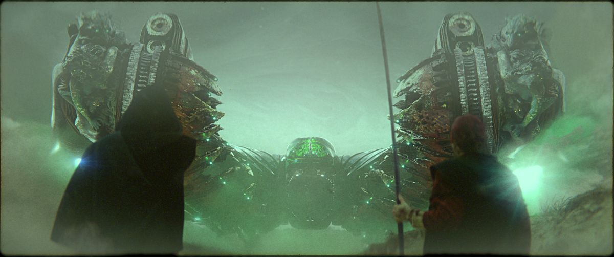 Two black-robed figures, one with a long staff, stand with their backs to the camera, facing a symmetrical spaceship backlit in green