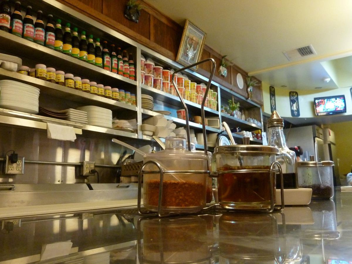 The counter at Rachawadee in Mount Vernon, Washington, with containers of spices in the foreground and shelves stocked with bottles of sauces and other sundries in the background