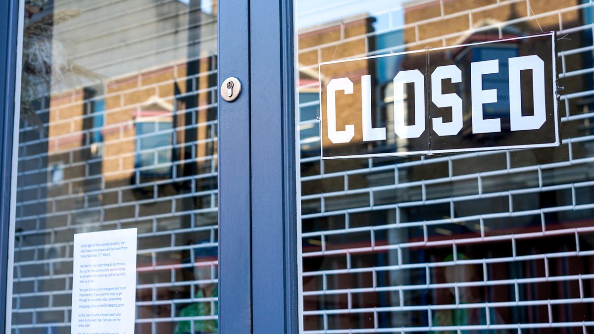 A closed sign hangs in the glass door of a restaurant in front of a closed security gate.