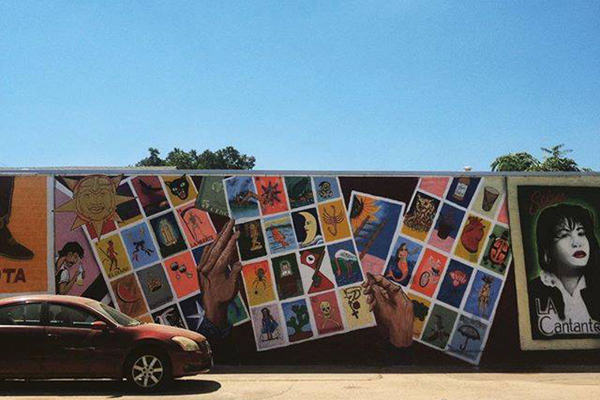 A building with Loteria game cards and Selena depicted on a mural with a car in front