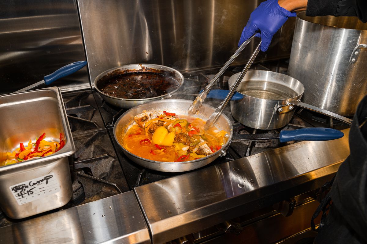 A cook uses tongs to move ingredients in a pan.