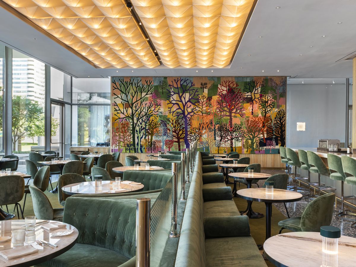 Le Jardinier’s plush dining room, with a tree-filled mural, suede-like green seats, and floor-to-ceiling windows.