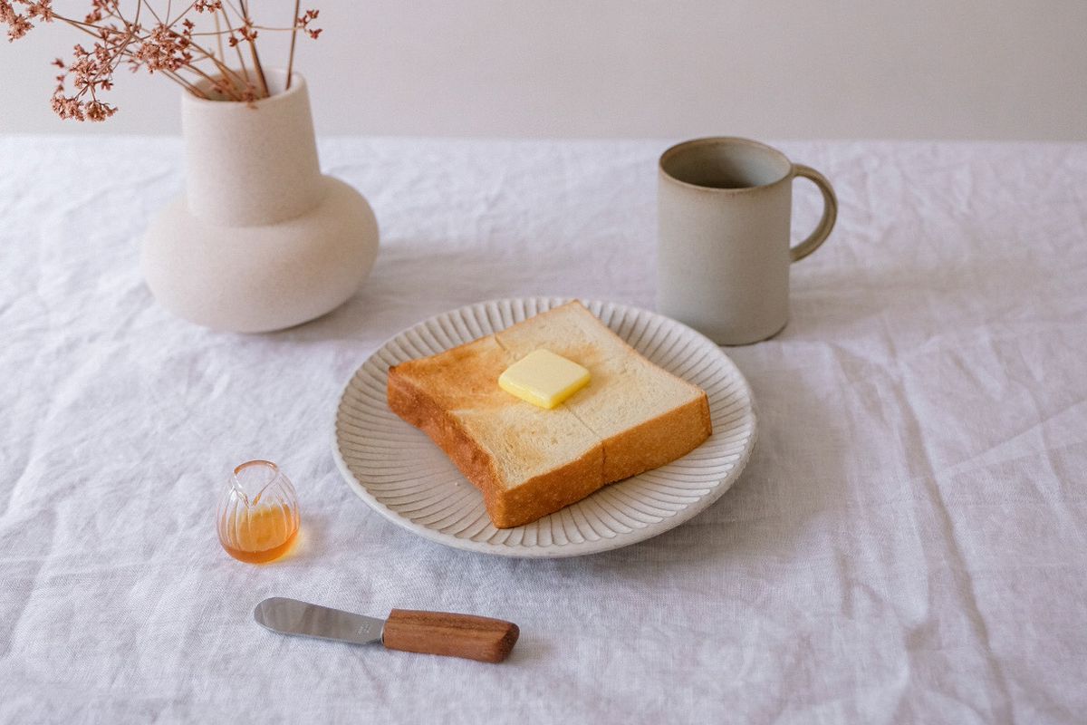A slice of buttered bread with coffee and a flowers in a vase.
