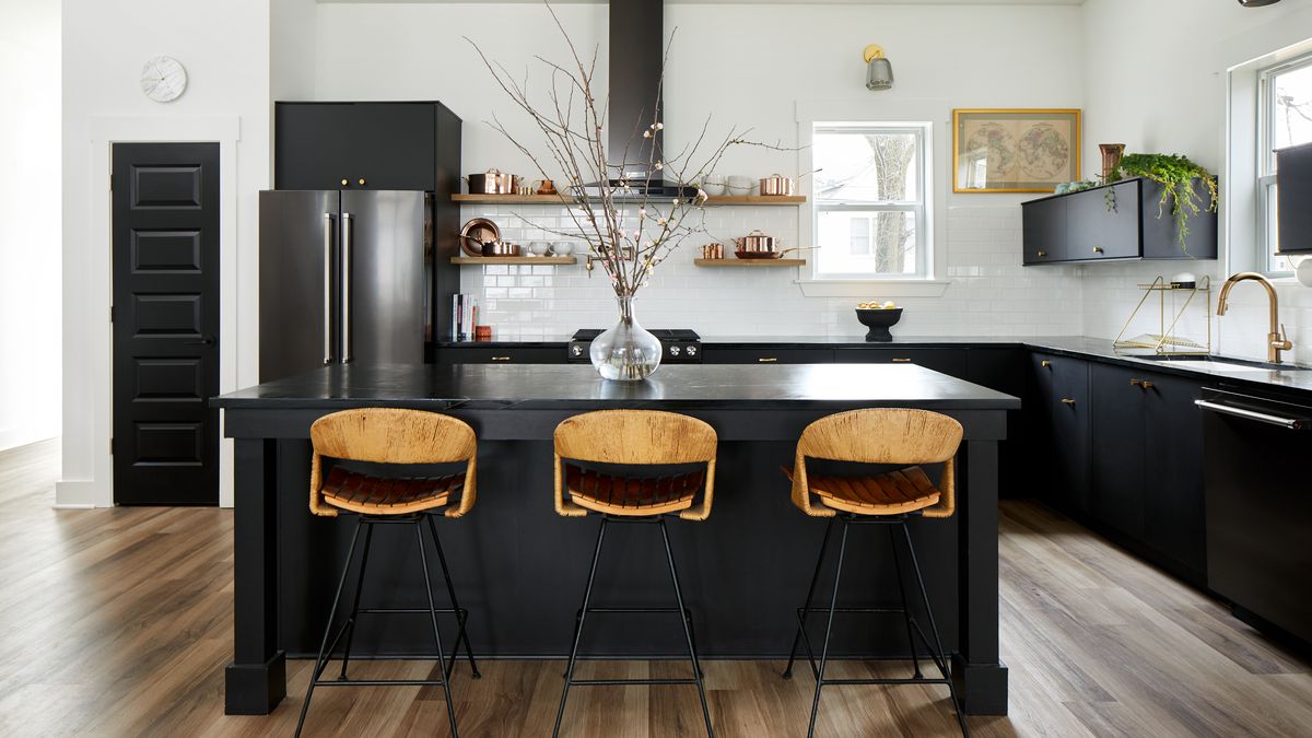 A kitchen with a wooden floor and a kitchen island with three chairs. The kitchen island and cabinets are painted black.