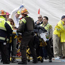 Two Boston Marathon volunteers hug each other, at right, as an injured person is loaded into an ambulance in the aftermath of two blasts which exploded near the finish line of the Boston Marathon in Boston, Monday, April 15, 2013. 
