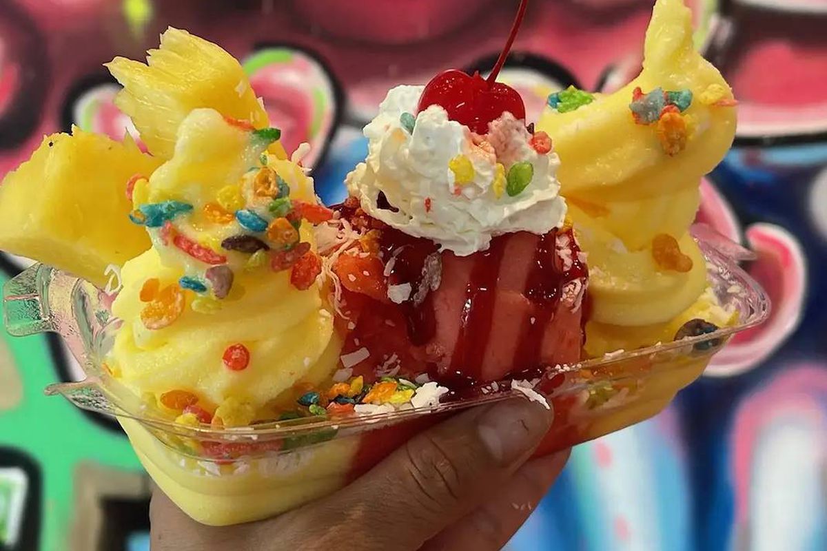 A banana split held in a hand with a swirling red and yellow background