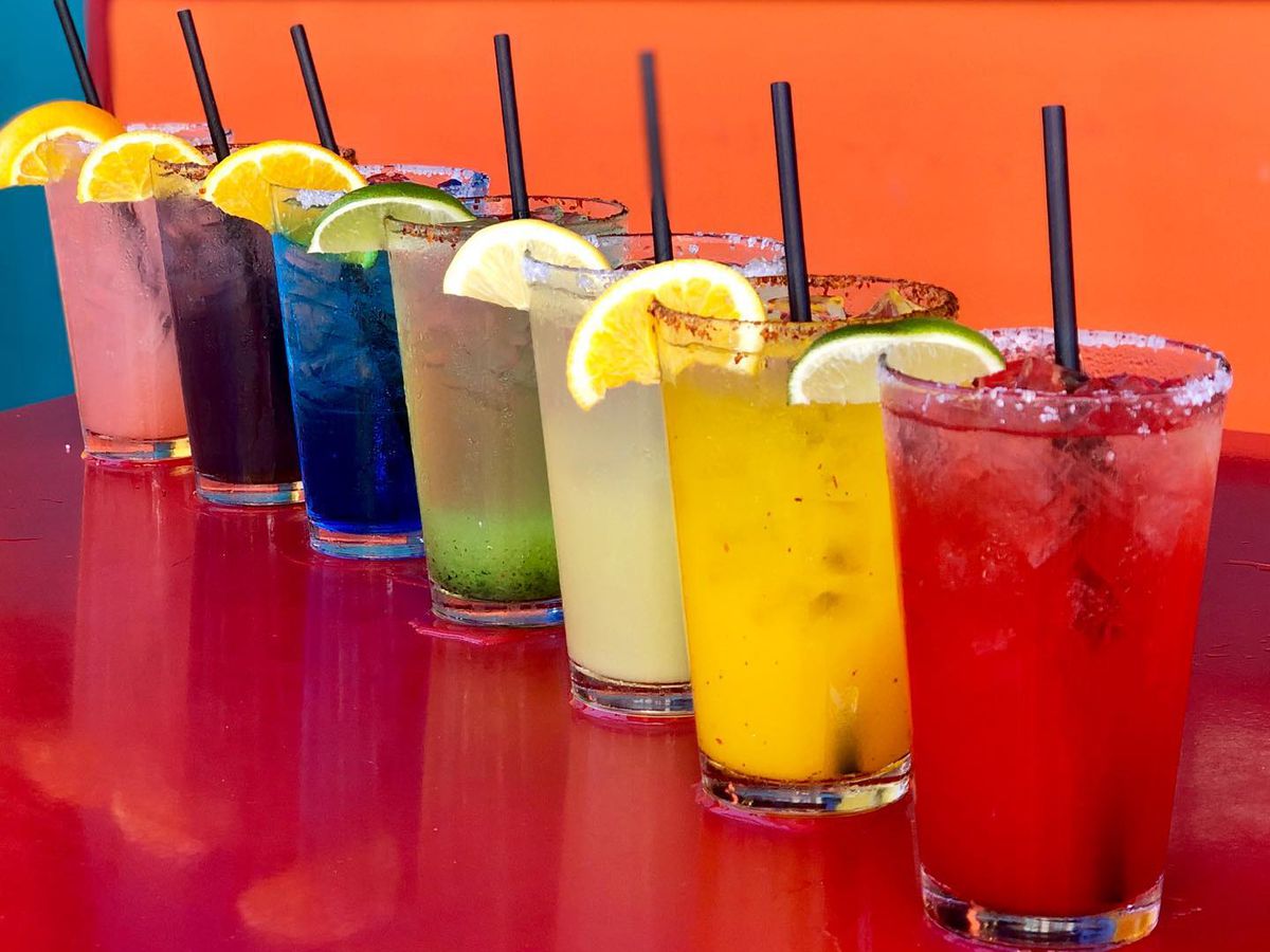 Rainbow of margaritas on red table.