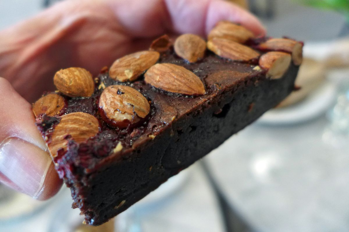 A dark chocolate brownie topped with whole almonds held between two fingers