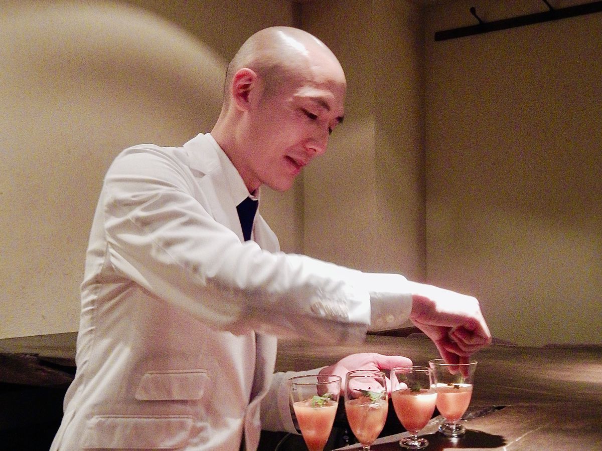 A bartender garnishes a row of cocktails on a dark wood bar.