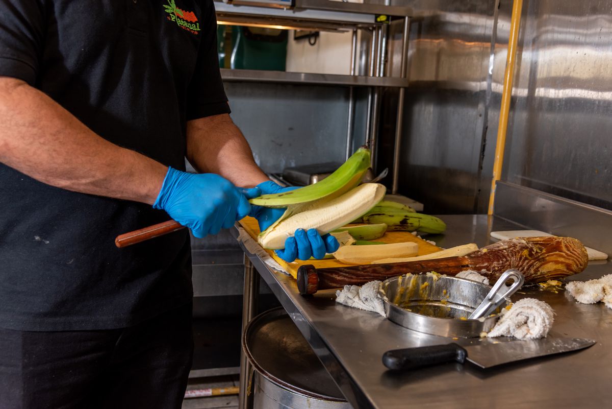 A chef peels a green plantain with a long knife. 