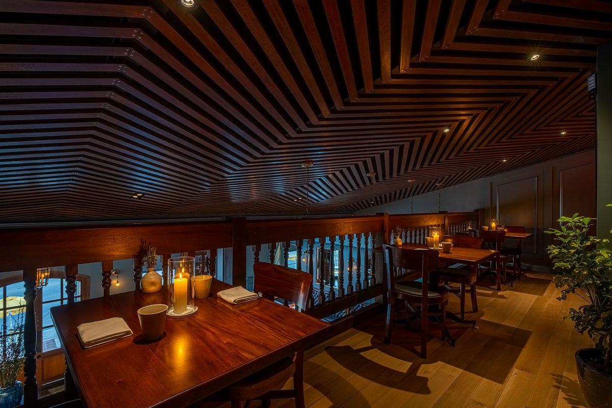 Wood tables, appointed candle and tablesettings on a mezzanine of a dimly lit restaurant.