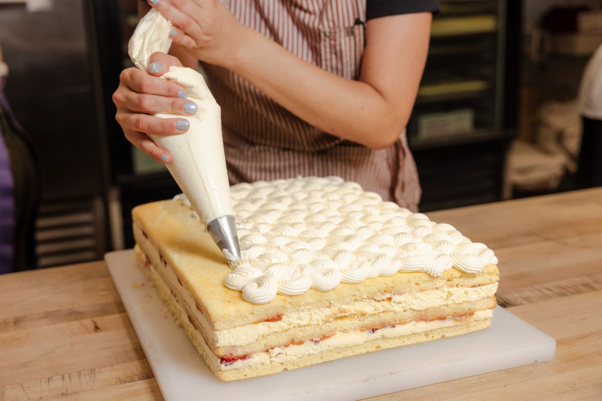 A person pipes cream onto a sheet cake.