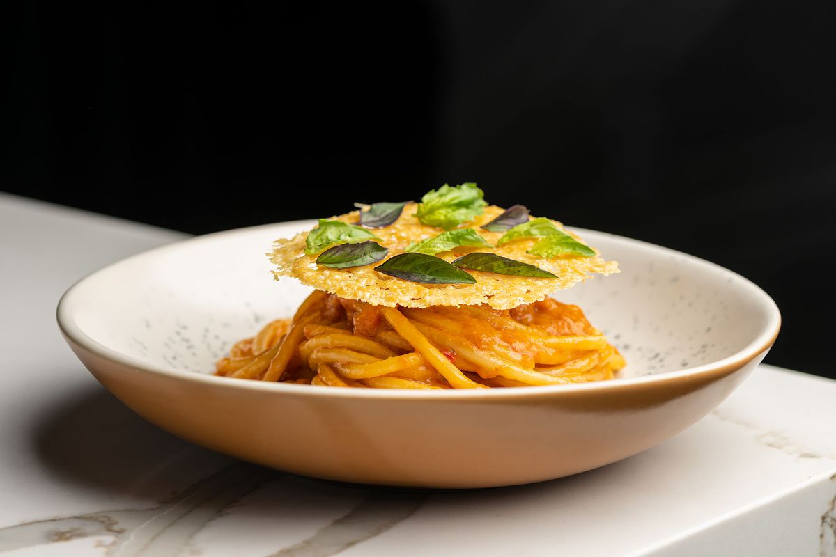 A plate of bucatini with tomato sauce and a parmesan crisp on top.