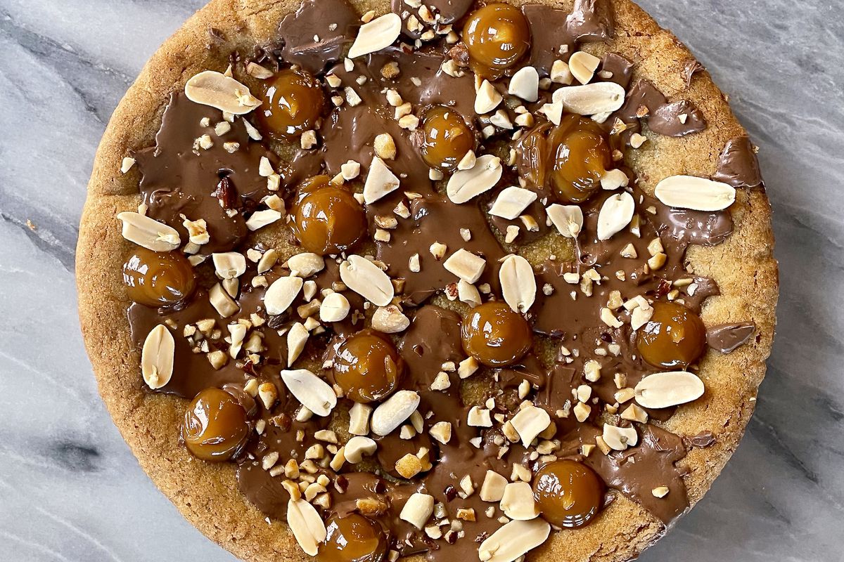 Cookie cake on a marble countertop with peanuts and a caramel spread.