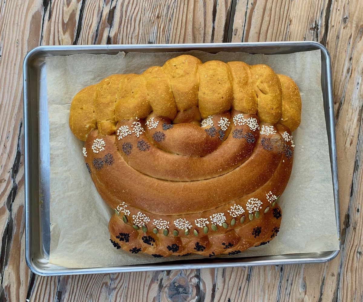 A silver tray atop a wooden table showing challah bread shaped like a traditional Hanukkah menorah.