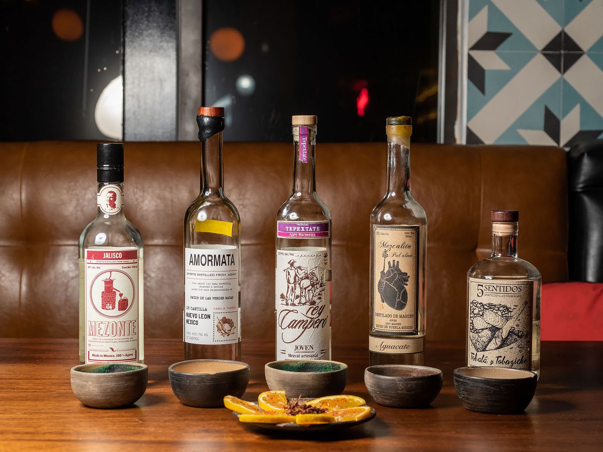 Five select artisan bottles from Madre in Torrance lined up with sliced oranges and chapulines.