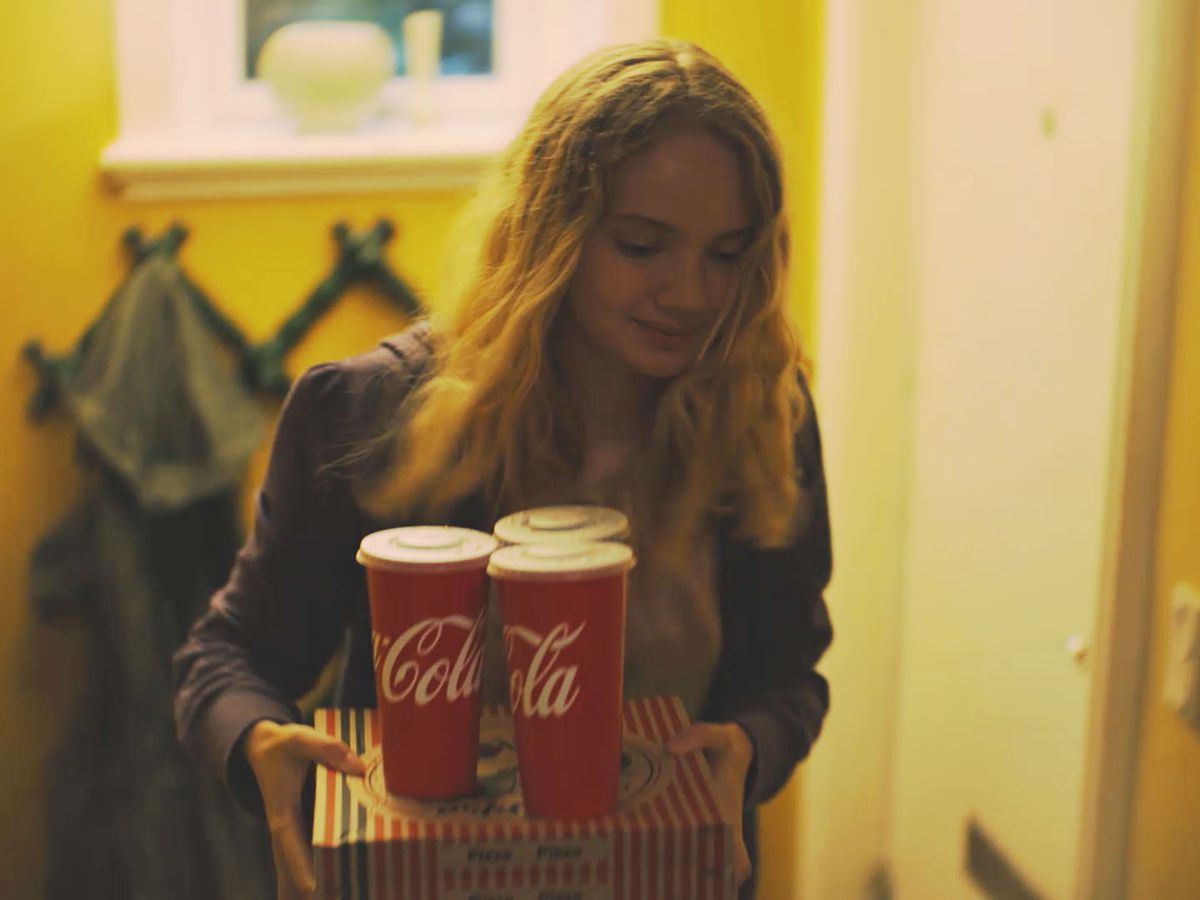 A young woman brings home a box of takeout food with three Coca-Colas in paper cups.