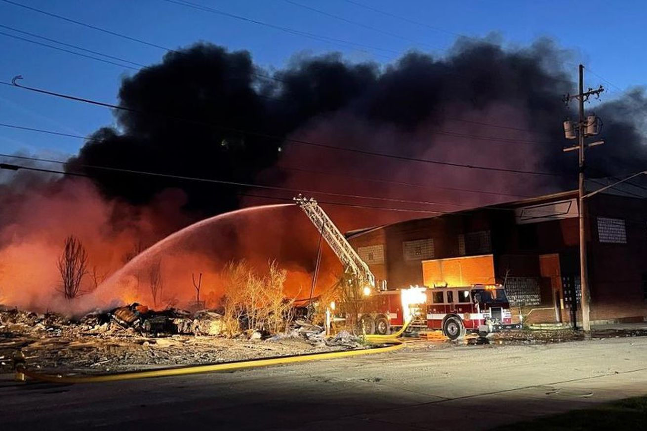 A firetruck houses water on burning rubble with a thick plume of smoke rising above.