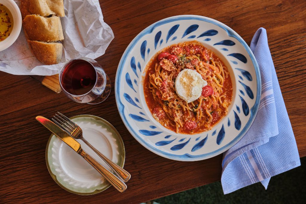This is a photo of spaghetti with tomato sauce. There is also cut slices of bread, a glass of red wine, a folded napkin, and silverware in the picture.