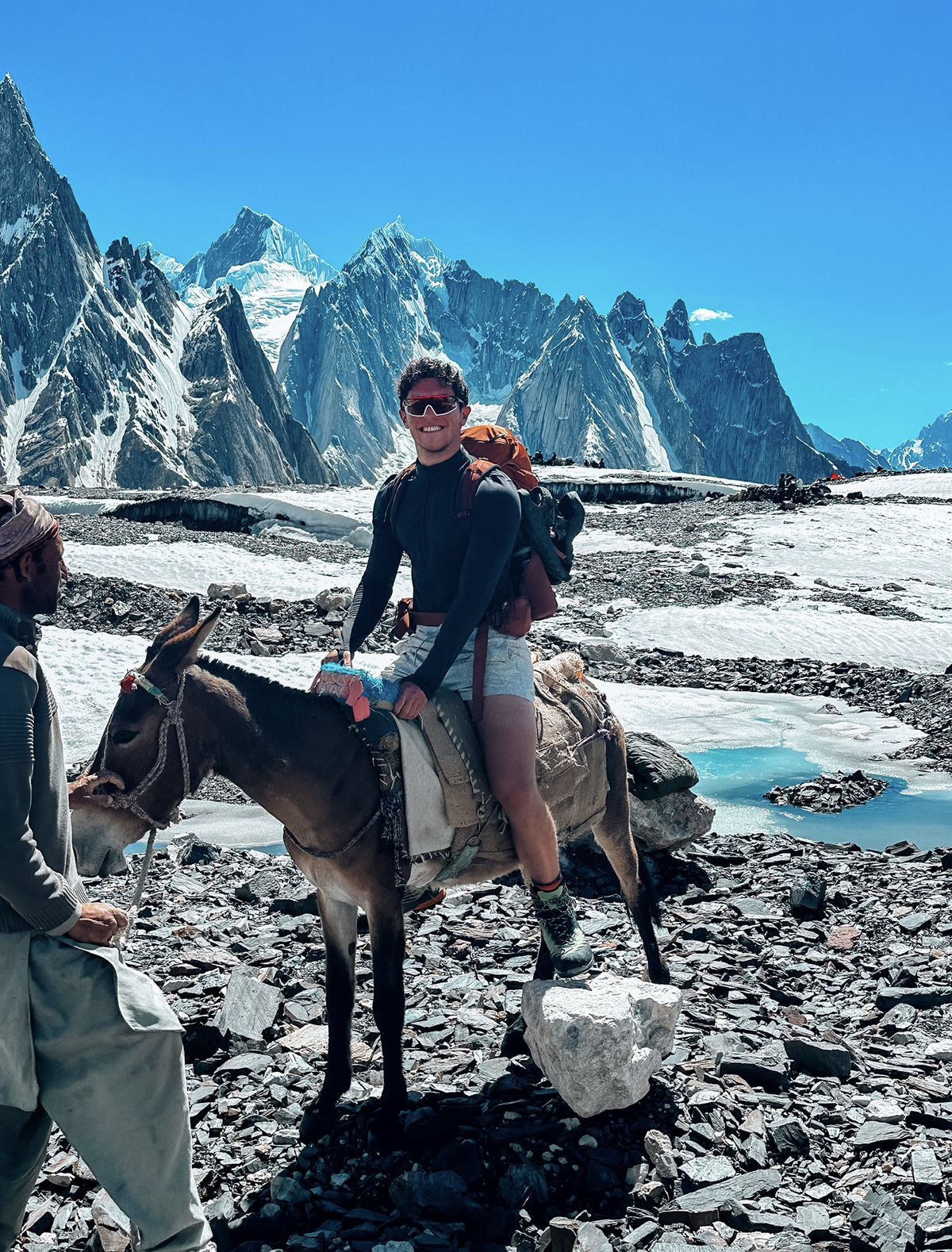 Mountain climber riding a donkey with mountains in background.