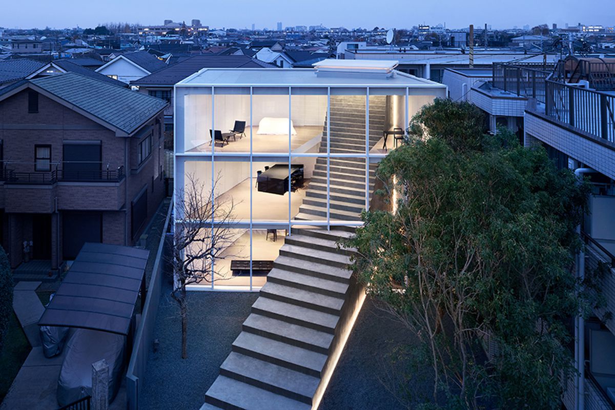 Exterior shot of house lit up at night with a huge staircase running through a glass facade.